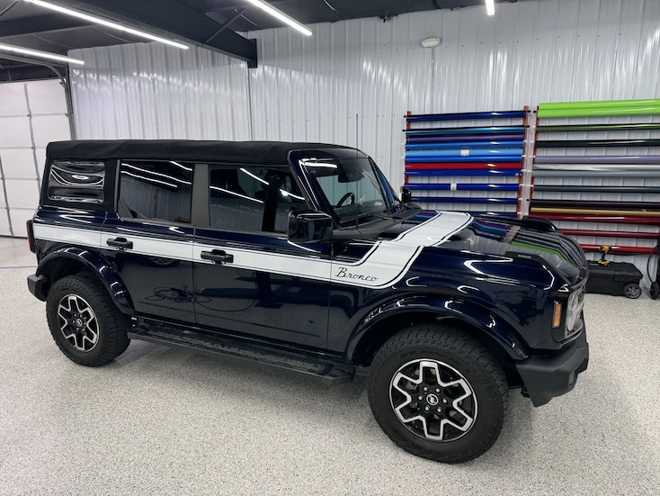 Dark blue Ford Bronco with custom white racing stripe in an auto shop setting.